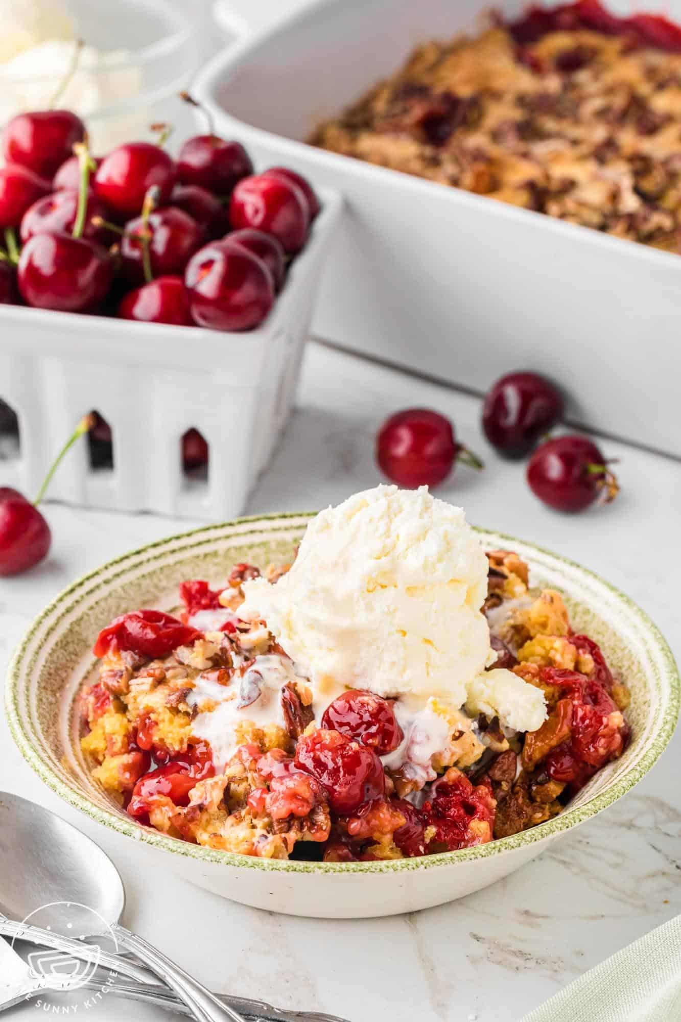Warm mini dump cake for two made with cherry pie filling and golden buttery cake topping served with melting vanilla ice cream in a small baking dish.